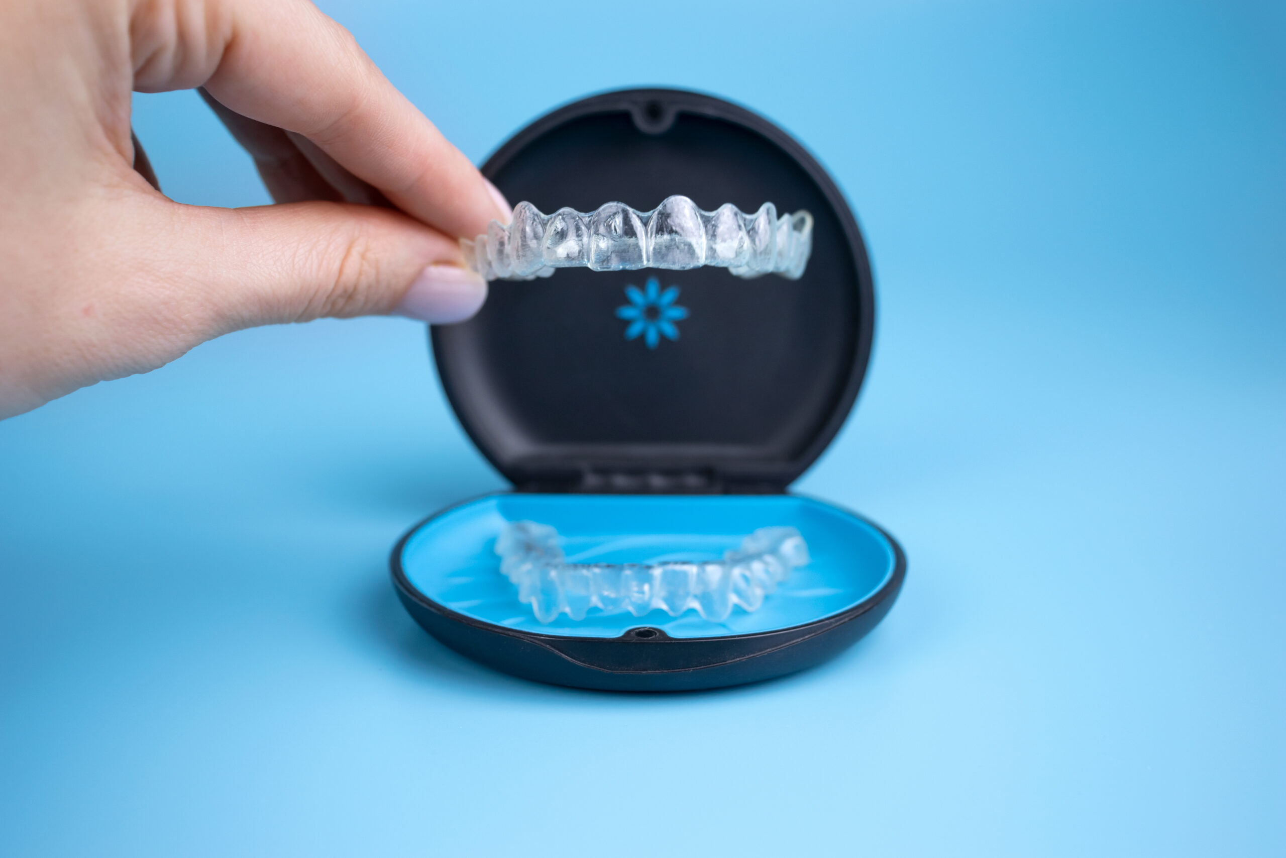 Woman holding invisalign transparent retainers with a box on the table, flatlay top view. Selective focus.
